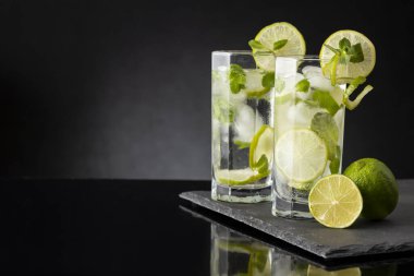 Beyaz rom, limon suyu ve limon dilimleri ve nane yapraklarıyla süslenmiş bir bardak soğuk mojito kokteyli. Daha yakın cama odaklan.