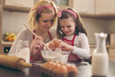 Genç anne mutfakta kızıyla hamur pişiriyor, anne unu karıştırırken kız da yumurta ekliyor. Annesine odaklan.