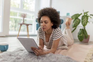 Kadın blogcu oturma odasında yerde yatıyor, yeni bir blog yazısı yazıyor, evden uzaktan çalışıyor.