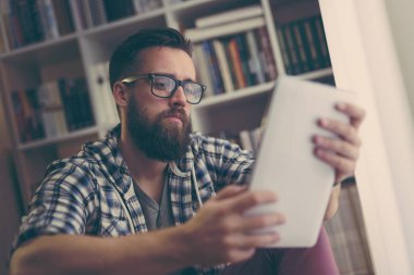 Yakışıklı bir adam kütüphanesinin zemininde oturuyor, tablet bilgisayarında internette geziniyor, boş zamanlarında dinleniyor.