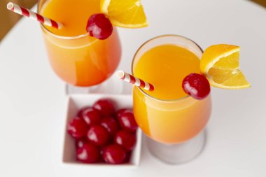 Yüksek açılı iki soğuk tekila kokteyli, tekila, nar suyu ve portakal suyu ile süslenmiş portakal suyu ve maraska kirazı. Camdaki kiraza odaklan.