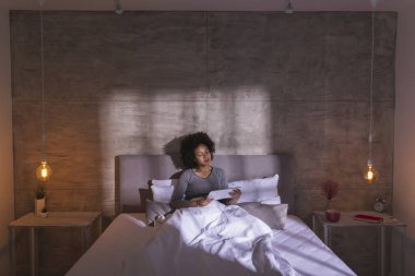 Pijama giymiş, internette tablet bilgisayar kullanarak gezinen ve sabahları evde dinlenen güzel melez bir kadın.