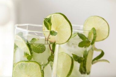 İki mojito kokteyli, bol buzlu, beyaz rom, limon suyu ve tonik, limon dilimleri ve nane yapraklarıyla süslenmiş. Nane yapraklarına ve bardaktaki limonlara odaklan.