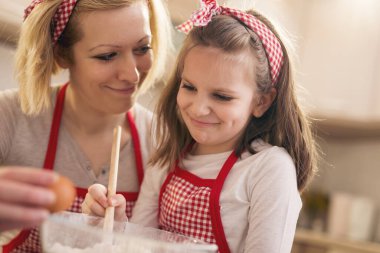 Genç anne mutfakta kızıyla hamur pişiriyor, kız unu karıştırırken yumurta kırıyor. Kızına odaklan.