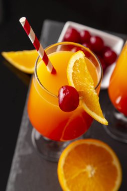 Yüksek açılı iki soğuk tekila kokteyli, tekila, nar suyu ve portakal suyu ile süslenmiş portakal suyu ve maraska kirazı. Camdaki kiraza odaklan.