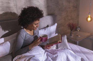 Sabahları pijama giyen, kitap okuyan ve çay içen genç ve güzel bir ırk kadını.