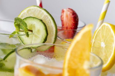 Taze çilek, kireç ve nane yaprağı, limon ve portakalla doldurulmuş su bardakları. Nane yaprağına ve camdaki salatalığa odaklan.