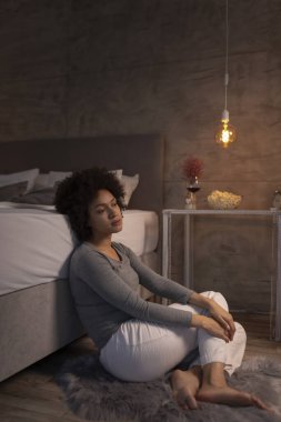 Güzel, melez bir ırk kadını pijama giyiyor, gece yatağında oturuyor, yoğun bir iş gününden sonra evde dinleniyor.