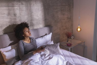 Güzel, genç, melez bir kadın. Sabahları yatakta uzanıyor. İnternette akıllı telefon kullanıyor ve evde dinleniyor.