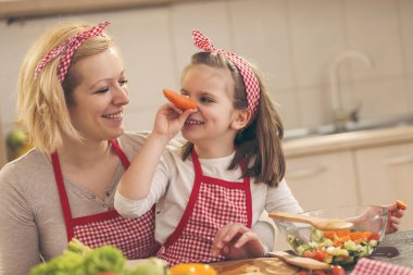 Güzel anne ve kız salata için sebze keserken mutfakta eğleniyorlar; kız havuç burnu yapıyor