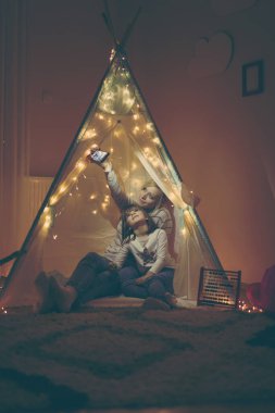 Anne ve kızı çadırda oturup selfie çekiyorlar ve oynuyorlar.