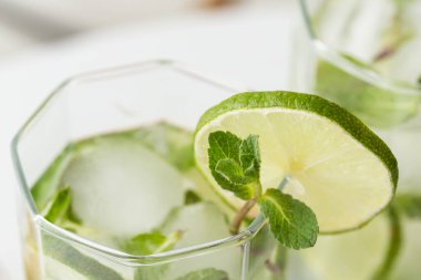 Yüksek açılı iki mojito kokteyli, bol buzlu, beyaz rom, limon suyu ve tonik, limon dilimleri ve nane yapraklarıyla süslenmiş. Nane yapraklarına odaklan
