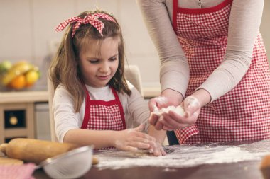 Little girl sprinkling flour over the kitchen table, helping her mother to bake a pizza dough