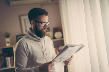 Düşünceli genç adam kütüphanesinde gazete okuyor.