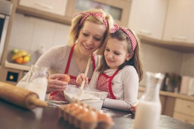 Genç anne mutfakta kızıyla hamur pişiriyor, kızı unu boğarken bir yumurta kırıyor. Kızına odaklan.