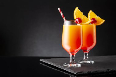 İki soğuk tekila gündoğumu kokteyli, tekila, nar suyu ve portakal suyu ile süslenmiş portakal suyu ve maraska kirazı.