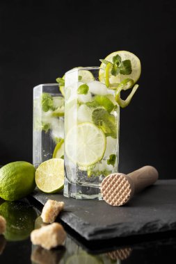 Beyaz rom, limon suyu ve limon dilimleri ve nane yapraklarıyla süslenmiş bir bardak soğuk mojito kokteyli.