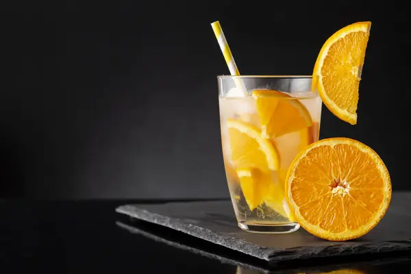 新鮮で冷たいガラスはオレンジ色のスライス アイスキューブ 黒い石造りのトレイの飲料のわらで水を注入しました 選択的なフォーカス — ストック写真