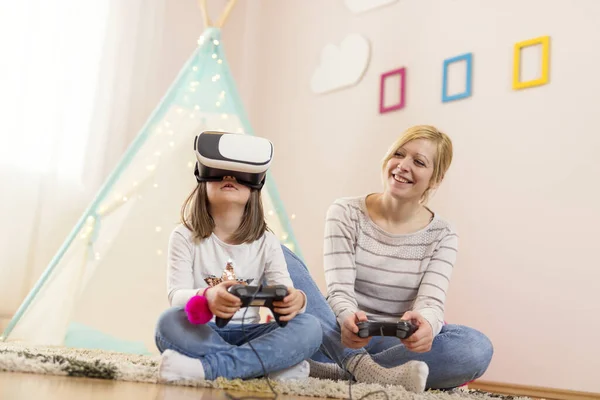 Mother and daughter sitting on the floor in a playroom, playing 3D VR game and having fun. Focus on the daughter