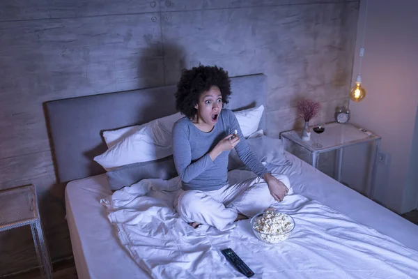 Piękna Mieszana Kobieta Rasy Piżamie Siedząca Łóżku Jedząca Popcorn Oglądająca — Zdjęcie stockowe
