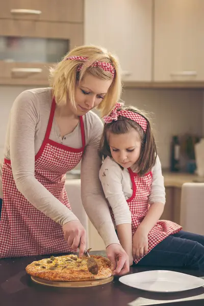 Anne ve kızı taze pişmiş pizzayı yemek için hazırlıyorlar. Annesine odaklan.