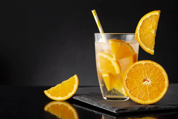 新鮮な 冷たい注入された水のガラス オレンジのスライス 氷の立方体および黒い石の皿の飲み物のわら — ストック写真