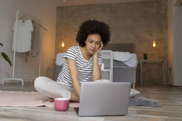 Female freelancer sitting on the bedroom floor, working on a laptop computer and drinking coffee; woman working remotely from home