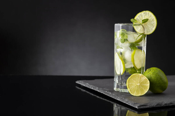 Mojito cocktail with lots of ice, white rum, lemon juice and tonic, decorated with lime slices and mint leaves on a black stone tray