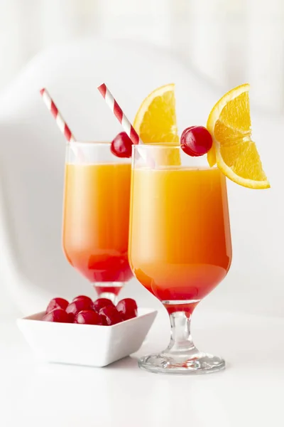 Two cold tequila sunrise cocktails with tequila, pomegranate juice and orange juice decorated with slices of orange and maraschino cherries