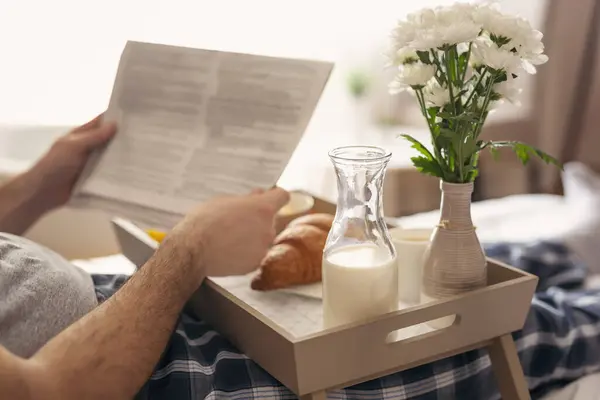 Man wearing pajamas, sitting in bed, reading newspapers and having breakfast. Selective focus on the milk bottle