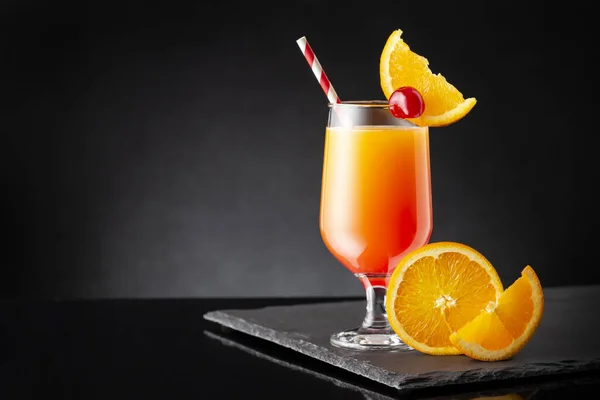 Cold tequila sunrise cocktail with tequila, pomegranate juice and orange juice decorated with slices of orange and maraschino cherries