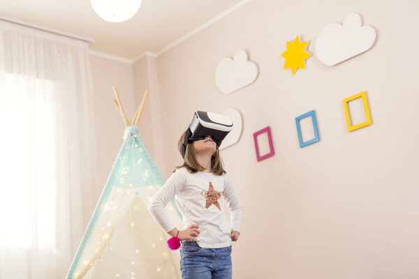 Маленькая девочка в наушниках виртуальной реальности, играет в игровой комнате и веселится