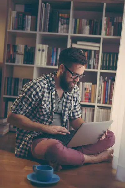 Yakışıklı Bir Adam Kütüphanesinin Zemininde Oturmuş Dizüstü Bilgisayarında Internette Geziniyor — Stok fotoğraf