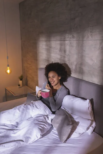 즐거운 레이스 침대에 잠옷을 전화로 말하고 커피를 마시고 아침에 집에서 — 스톡 사진