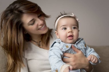Genç anne kucağında bebeğini kucağında tutuyor, oynuyor ve anneliğin tadını çıkarıyor.