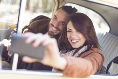 Genç çift yol gezisinde güneşli günün tadını çıkarıyor ve eğleniyor, selfie çekiyor.. 