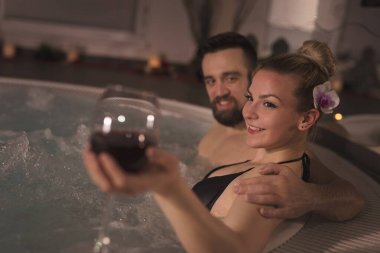 Aşık bir çift jakuzinin romantik atmosferinin tadını çıkarıyor, şarap içiyor ve dinleniyor.