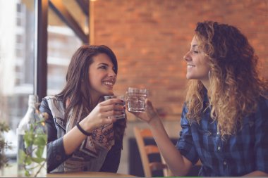 İki kız bir kafede oturmuş, nane yapraklarıyla detoks suyu içip eğleniyorlar. Soldaki kıza odaklan.