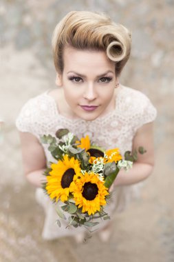 Gelinlik giymiş genç ve güzel bir gelinin kaldırım yolunda dikilip elinde bir buket ayçiçeği tutmasının en güzel görüntüsü.