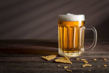 Çuval bezi örtüsüne konmuş bir kupa soğuk soluk bira ve kırsal ahşap bir masada biraz tortilla cipsi. Seçici odak