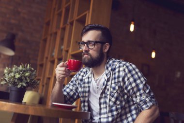 Yakışıklı genç adam bir kafede oturuyor, elinde bir fincan kahve tutuyor ve günün başlangıcından zevk alıyor.
