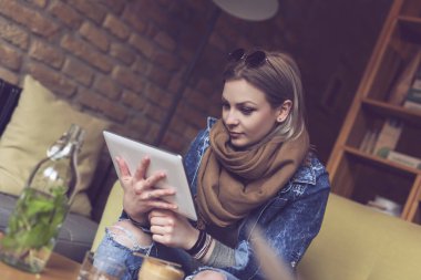 Güzel genç bir kadın bir kafede oturmuş, kahve içiyor ve internetteki bir tablet bilgisayarda sörf yaparken haberleri okuyor.
