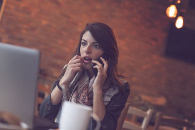 Çekici genç esmer bir kadın bir kafede oturuyor ve telefon görüşmesi yapıyor.