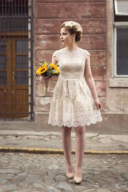 Güzelim gelin, elinde ayçiçeği buketi olan eski bir kaldırım kaldırımında gelinlik giymiş poz veriyor.