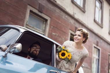Eski model bir arabada genç bir çift, gelin balayına çıkarken camdan el sallarken damat sürüyor. Geline odaklan.