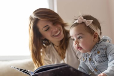 Genç anne kızına kitap okuyor, gülümsüyor ve harika annelik anları yaşıyor.