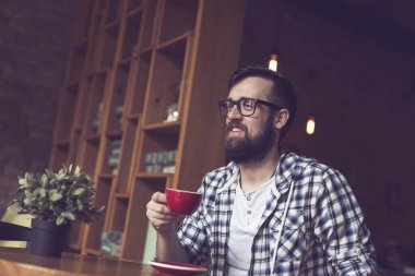 Yakışıklı genç hippi bir kafede oturuyor, sabah kahvesini içiyor, gülümsüyor ve uzaklığa bakıyor.