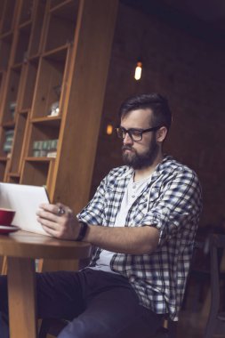 Yakışıklı genç hippi bir kafede dalgın dalgın oturuyor, sabah kahvesini içiyor, elinde bir tablet bilgisayar tutuyor ve internete yüklüyor.