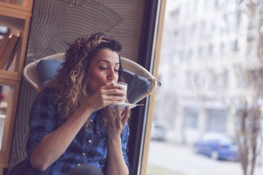 Güzel genç bir kadın bir kafede oturuyor, sabah kahvesinin tadını çıkarıyor.