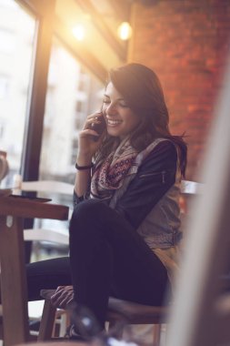 Çekici genç esmer bir kadın bir kafede oturuyor ve telefon görüşmesi yapıyor.